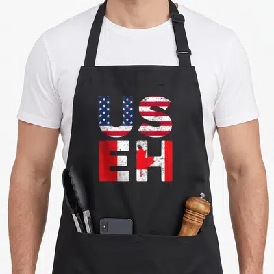 Useh pride apron - Stacked US and EH text with distressed US and Canadian flag patterns in red, white, and blue — shown on a black cotton canvas apron against a white background