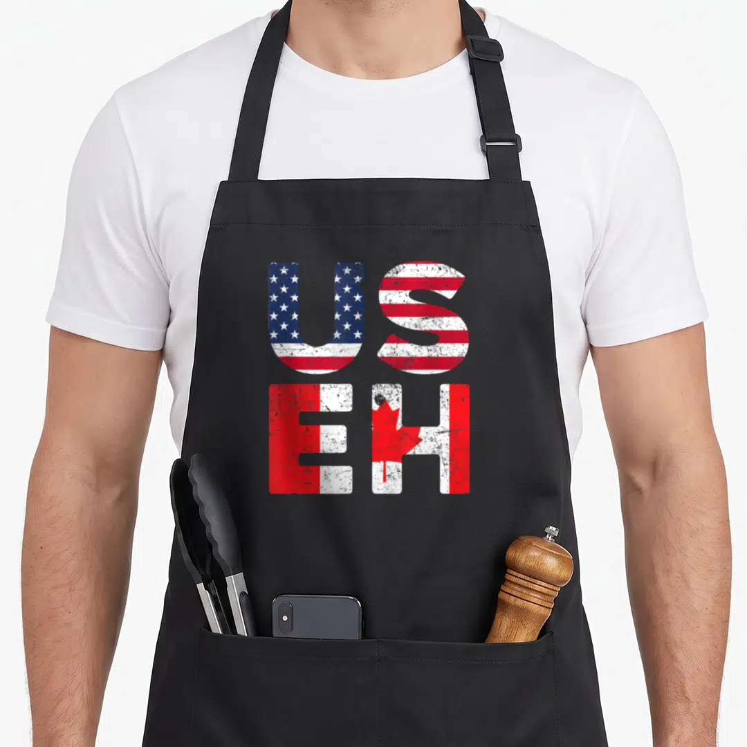 Useh pride apron - Stacked US and EH text with distressed US and Canadian flag patterns in red, white, and blue — shown on a black cotton canvas apron against a white background