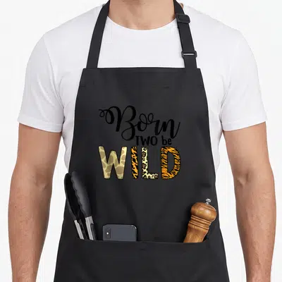 Nature 2nd apron - Born TWO be WILD text with giraffe leopard and tiger patterns inside letters — shown on a black cotton canvas apron against a white background