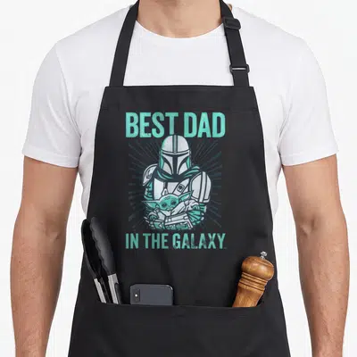 Galaxy gerbil dad apron - Cartoon Mandalorian holding Grogu with mint green text BEST DAD IN THE GALAXY and grey — shown on a black cotton canvas apron against a white background