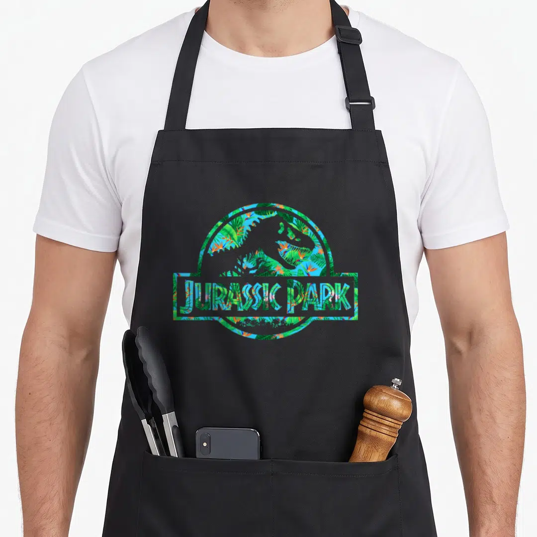 Tropical science apron - Dinosaur silhouette in circle filled with blue green orange tropical flora and JURASSIC PARK — shown on a black cotton canvas apron against a white background
