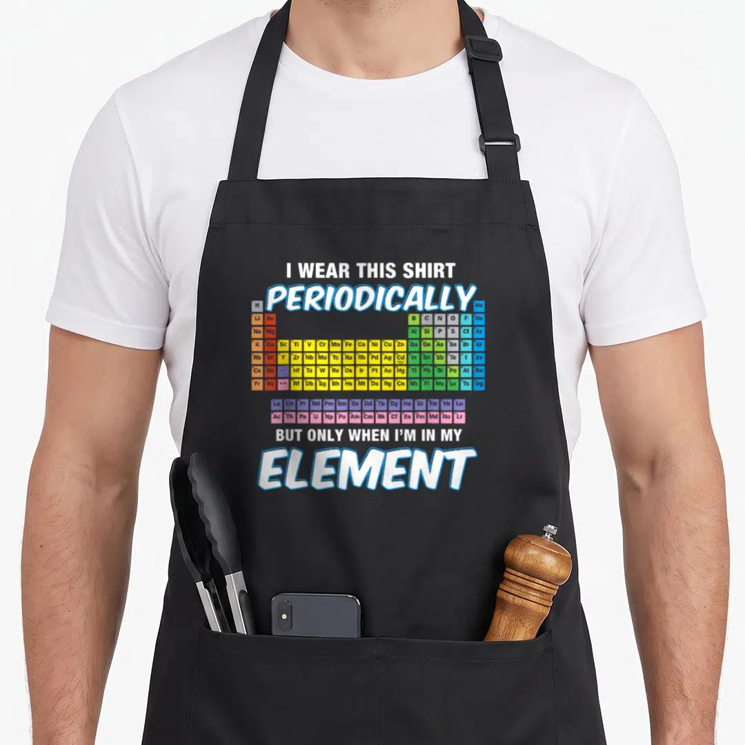 Perdion table apron - Periodic table chart with text I wear this shirt periodically but only when Im in my element — shown on a black cotton canvas apron against a white background