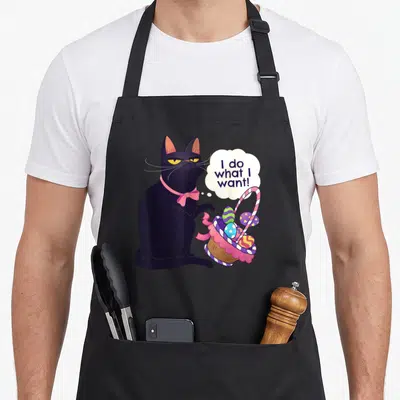 Cat easter basket apron - Grumpy black cat tipping Easter basket with speech bubble reading I do what I want — shown on a black cotton canvas apron against a white background