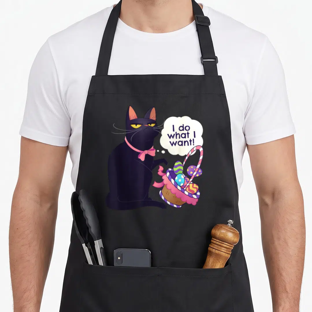 Cat easter basket apron - Grumpy black cat tipping Easter basket with speech bubble reading I do what I want — shown on a black cotton canvas apron against a white background
