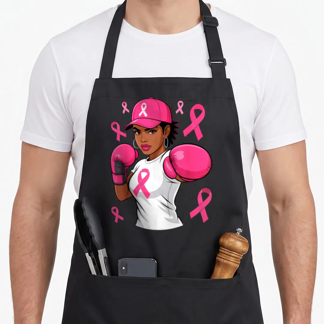 African ribbon apron - Cartoon woman with pink cap, boxing gloves, white shirt with pink ribbon, and floating pink — shown on a black cotton canvas apron against a white background