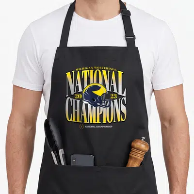 Cfp michigan boy apron - Yellow and navy blue football helmet with National Champions 2023 text — shown on a black cotton canvas apron against a white background