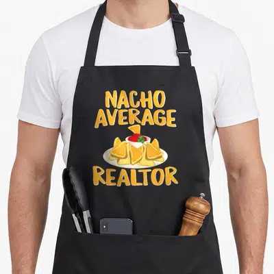 Nacho agent apron - Orange text reading Nacho Average Realtor above a plate of chips with red salsa and green garnish — shown on a black cotton canvas apron against a white background