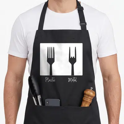 Heavy punk rock apron - Grey plastic and metal fork silhouettes with white script text on white rectangle — shown on a black cotton canvas apron against a white background