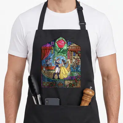 Enchanted stained apron - Dancing couple in stained glass with rose stem, crown, and background characters in blue — shown on a black cotton canvas apron against a white background