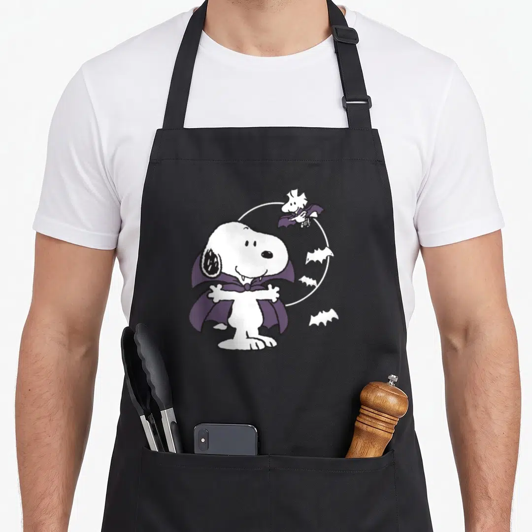 Funny vampire halloween apron - Snoopy vampire with purple cape, white moon, Woodstock as bat, cartoon style — shown on a black cotton canvas apron against a white background