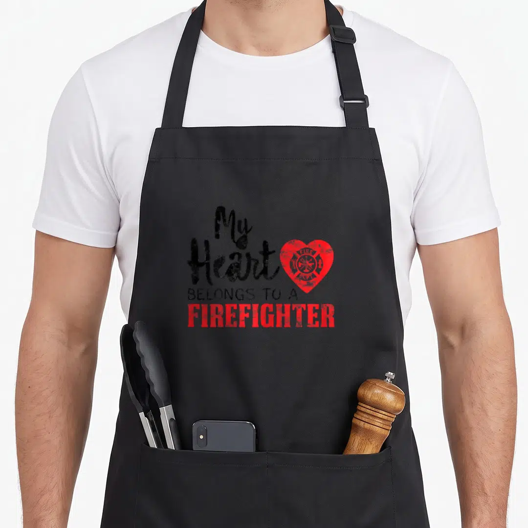 Fireman wife apron - Red heart with fire emblem and My Heart Belongs to a Firefighter text — shown on a black cotton canvas apron against a white background