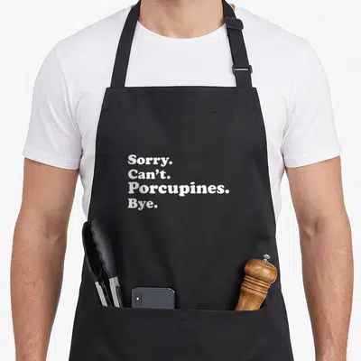 Porcupine apron or apron - White text reading Sorry Can't Porcupines Bye stacked on black background — shown on a black cotton canvas apron against a white background