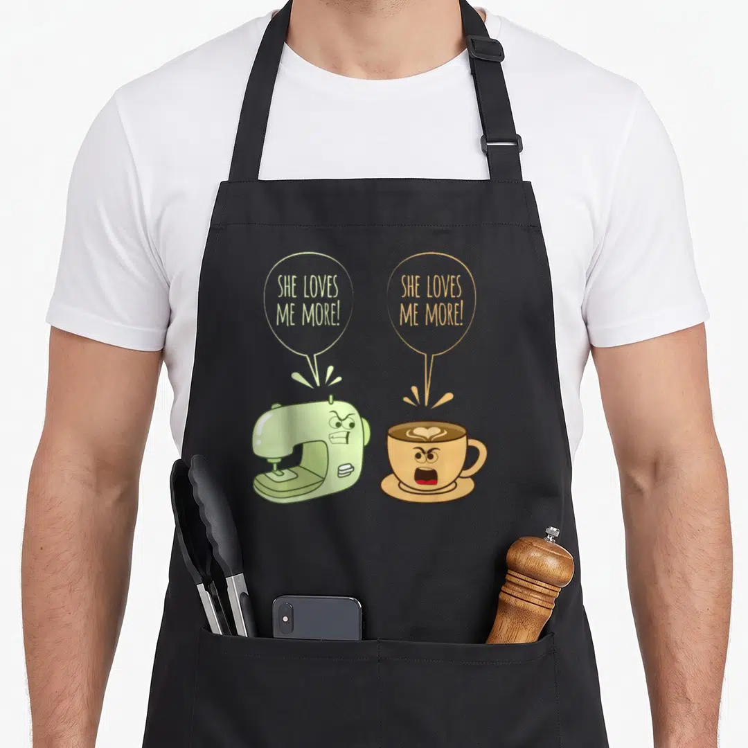 Sewing coffee apron - Cartoon sewing machine and coffee cup arguing SHE LOVES ME MORE in green and brown — shown on a black cotton canvas apron against a white background