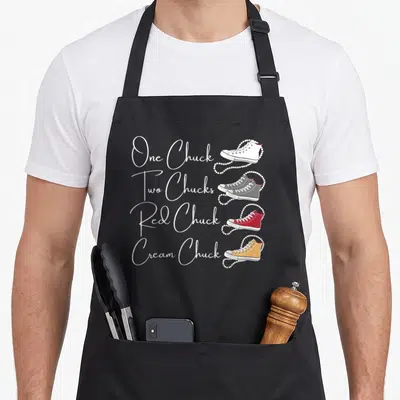 Pearl magic apron - Four sneakers in white grey red and yellow with pearl strings and matching text labels — shown on a black cotton canvas apron against a white background