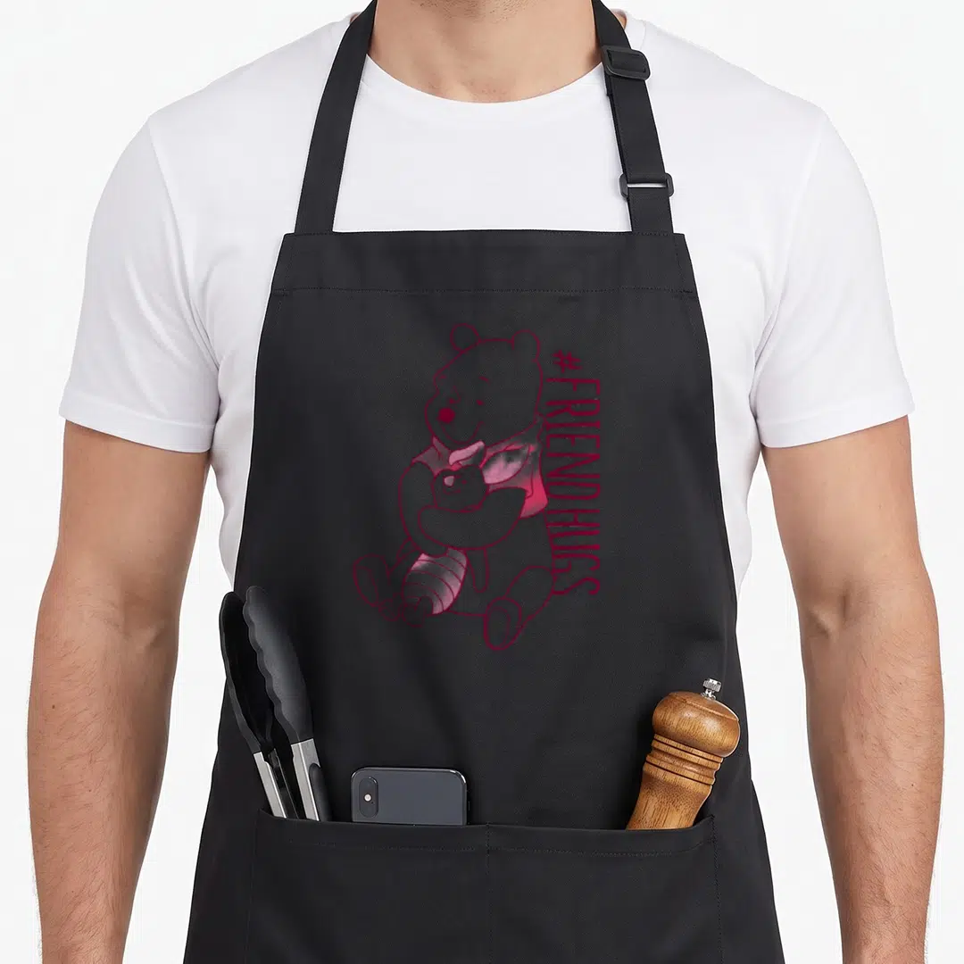 Hug friends apron - Winnie the Pooh hugging Piglet in dark pink line-art beside vertical #FRIENDHUGS text — shown on a black cotton canvas apron against a white background