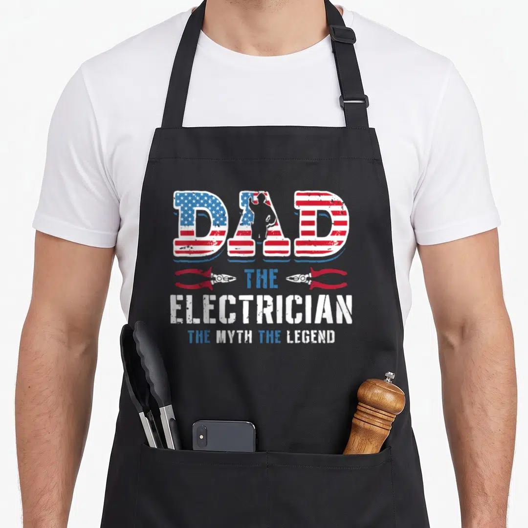 Myth electricians apron - DAD THE ELECTRICIAN THE MYTH THE LEGEND text with pliers and distressed flag pattern — shown on a black cotton canvas apron against a white background