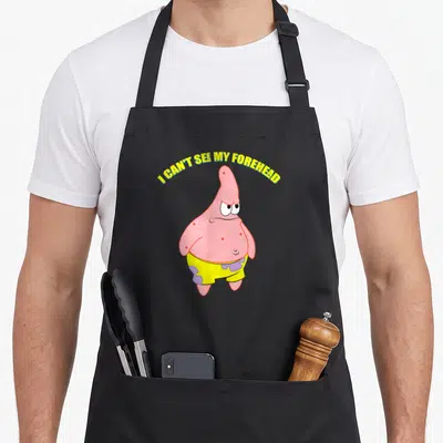 See star apron - Pink cartoon starfish wearing yellow shorts under arched yellow text reading I Can't See My Forehead — shown on a black cotton canvas apron against a white background