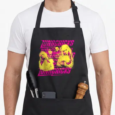 Lunachick novelty apron - Four yellow women clustered behind repeating pink JUNOWAVES text in retro style — shown on a black cotton canvas apron against a white background