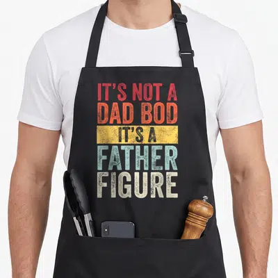 Father dad bod apron - Stacked red orange blue and white text reading IT'S NOT A DAD BOD IT'S A FATHER FIGURE — shown on a black cotton canvas apron against a white background