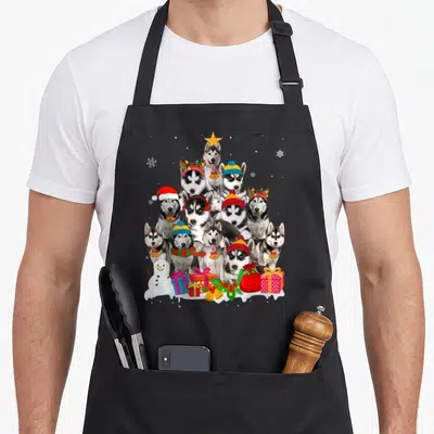 Christmas husky apron - Ten huskies in pyramid tree with snowman gifts grey white red blue yellow photo style — shown on a black cotton canvas apron against a white background