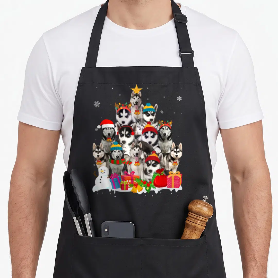 Christmas husky apron - Ten huskies in pyramid tree with snowman gifts grey white red blue yellow photo style — shown on a black cotton canvas apron against a white background