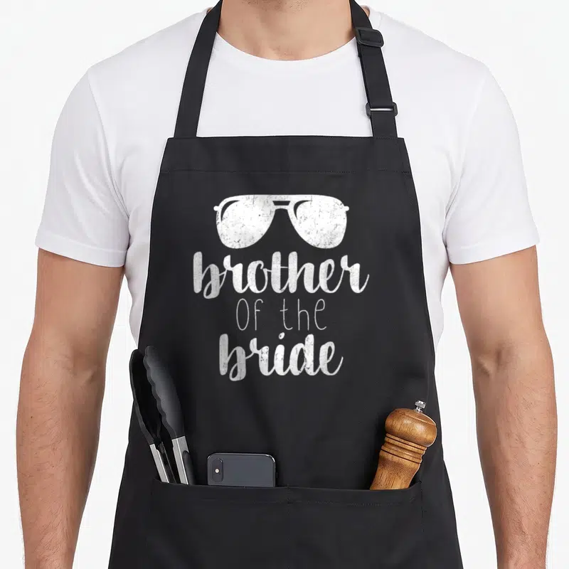 Brother bridal apron - White distressed sunglasses above stacked brother Of the bride text on black fabric — shown on a black cotton canvas apron against a white background