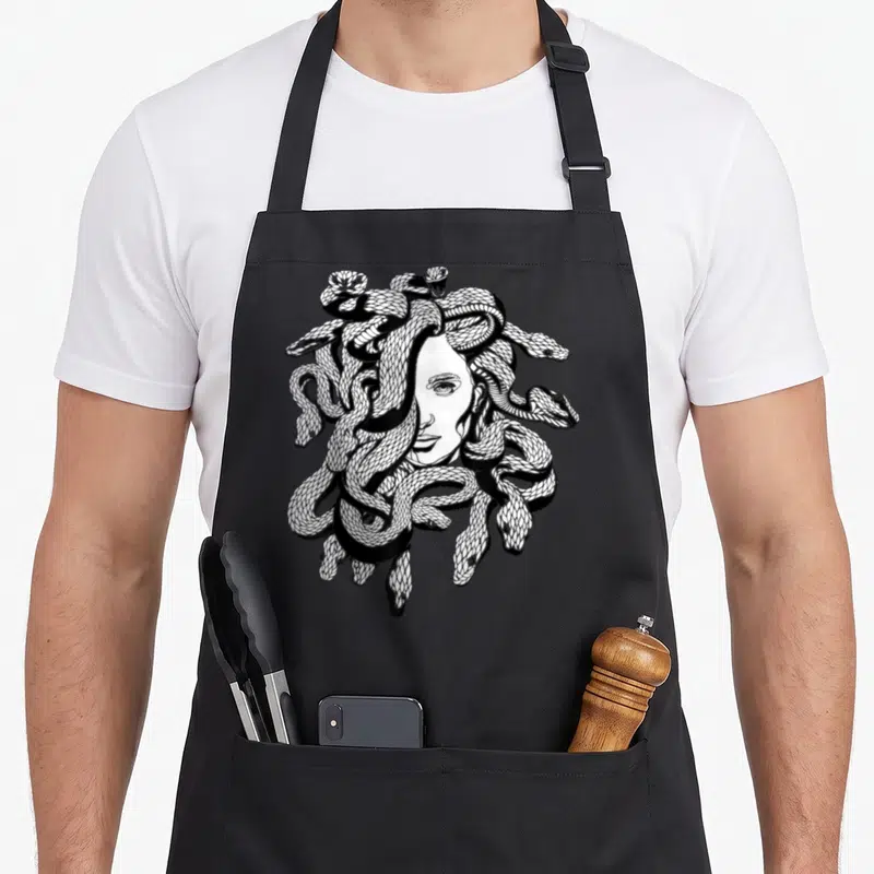 Snake greek aprons - Medusa face with snake hair in black and white line art — shown on a black cotton canvas apron against a white background