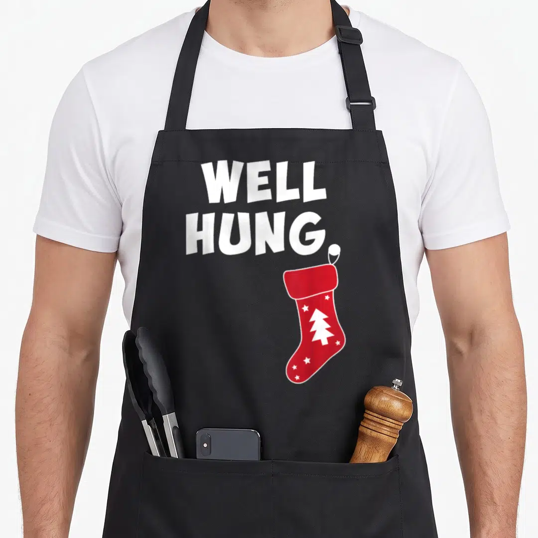 Dirty womens christmas aprons - Red Christmas stocking with white tree and stars below stacked white text reading well — shown on a black cotton canvas apron against a white background