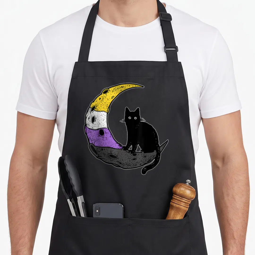 Nonbinary space cat apron - Black cat sits on crescent moon with yellow white purple grey bands, cartoon style — shown on a black cotton canvas apron against a white background