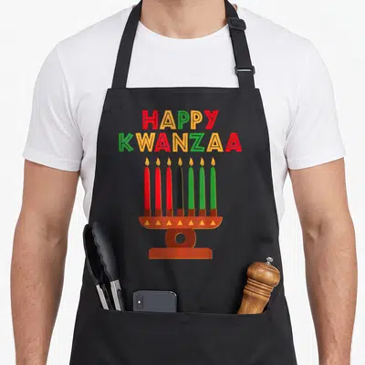 Kinara seven african american aprons - Happy Kwanzaa text above a kinara with seven red black and green candles — shown on a black cotton canvas apron against a white background