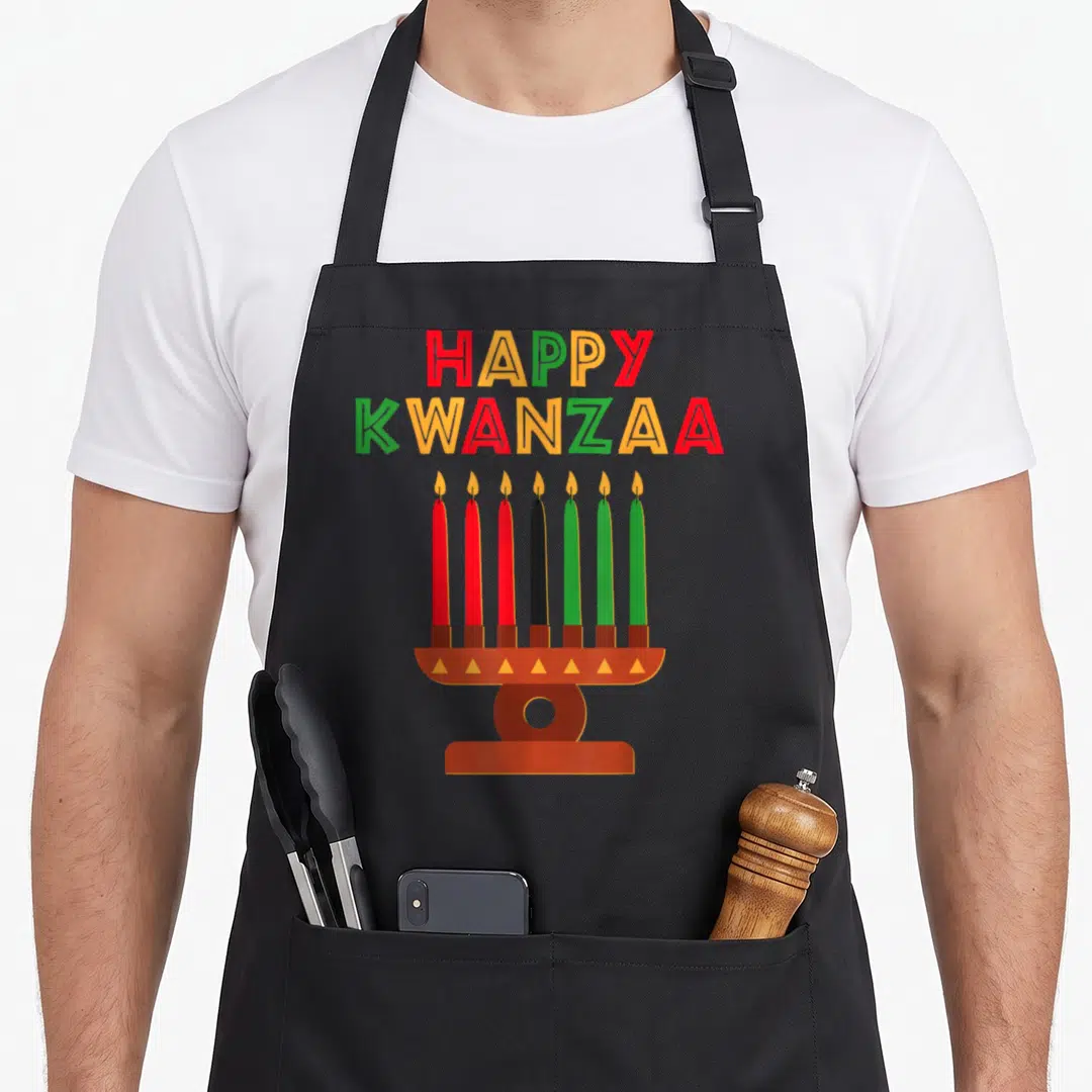 Kinara seven african american aprons - Happy Kwanzaa text above a kinara with seven red black and green candles — shown on a black cotton canvas apron against a white background