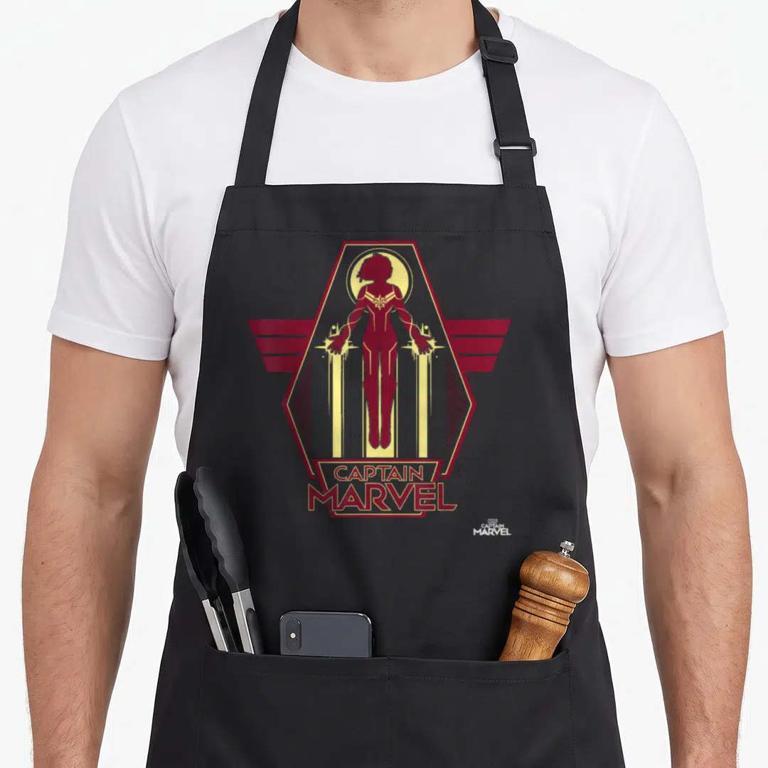 Flight captain apron - Red Captain Marvel silhouette in yellow hexagon with banner text — shown on a black cotton canvas apron against a white background