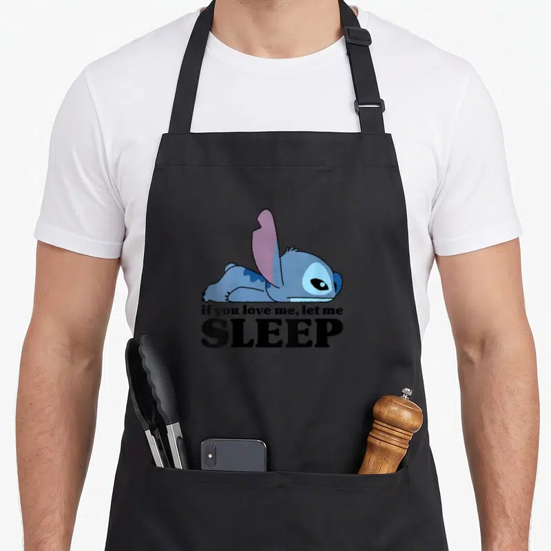 Funny sleepy stitch apron - Blue character lying down below if you love me, let me SLEEP text — shown on a black cotton canvas apron against a white background