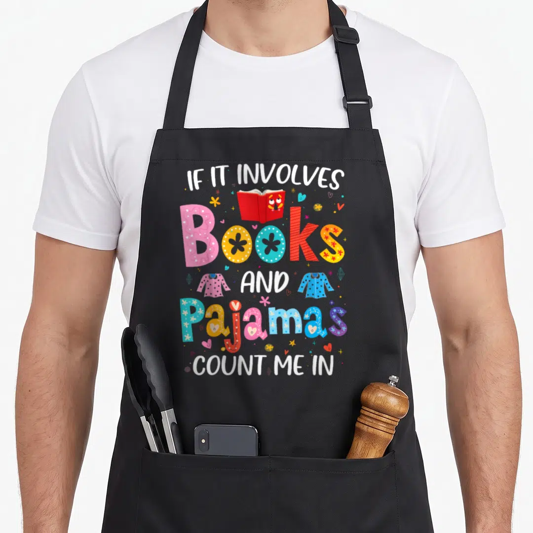 Involve pajama day apron - Stacked text reading If It Involves Books And Pajamas Count Me In with cartoon book — shown on a black cotton canvas apron against a white background