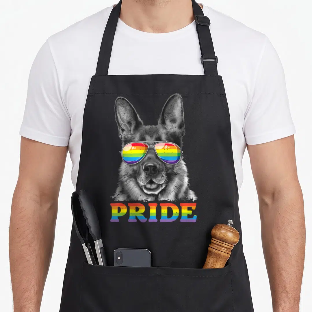Shepherd gay pride apron - Grayscale German Shepherd head wearing rainbow aviator sunglasses above rainbow PRIDE text — shown on a black cotton canvas apron against a white background
