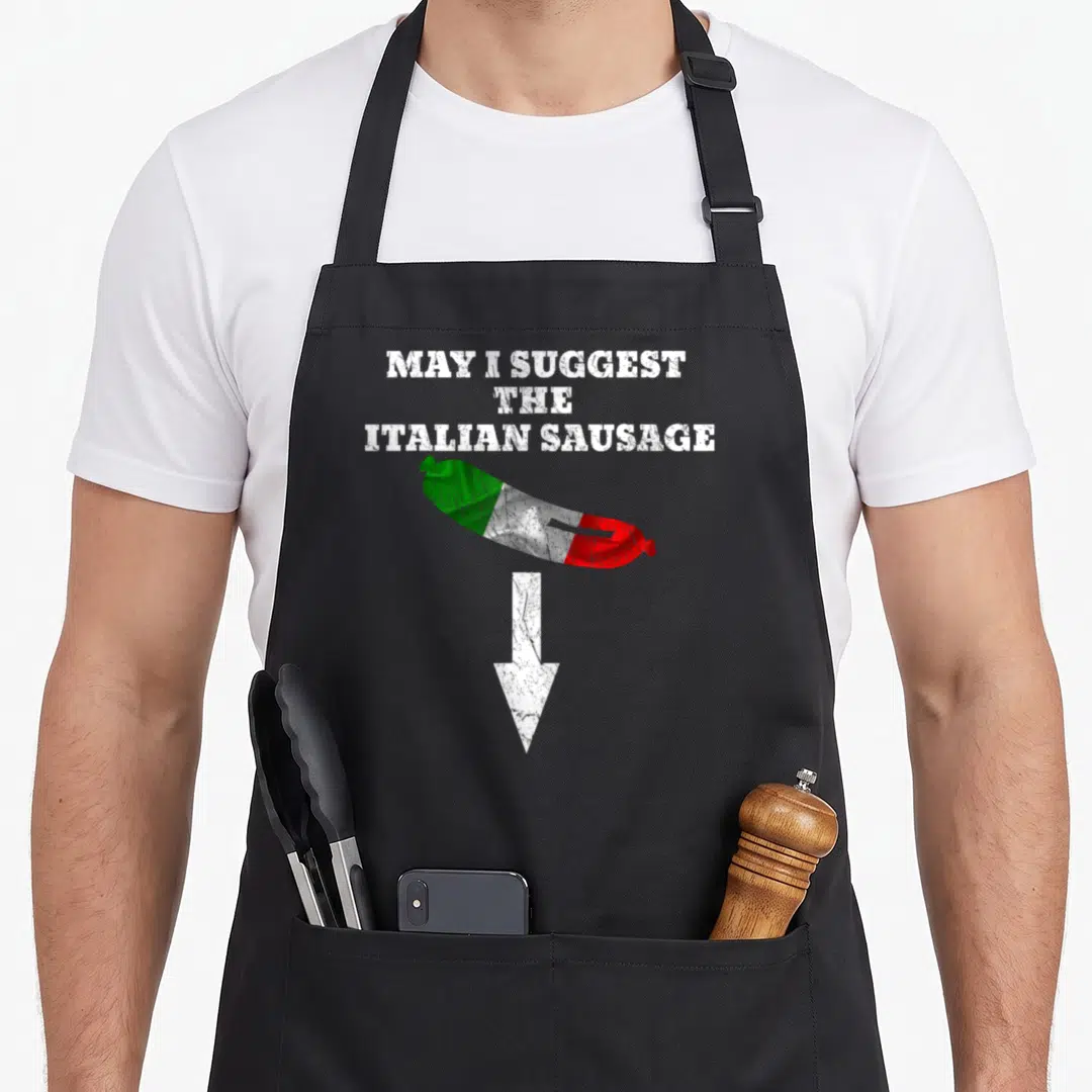 Naughty sausage apron - MAY I SUGGEST THE ITALIAN SAUSAGE text with flag-colored sausage and arrow — shown on a black cotton canvas apron against a white background