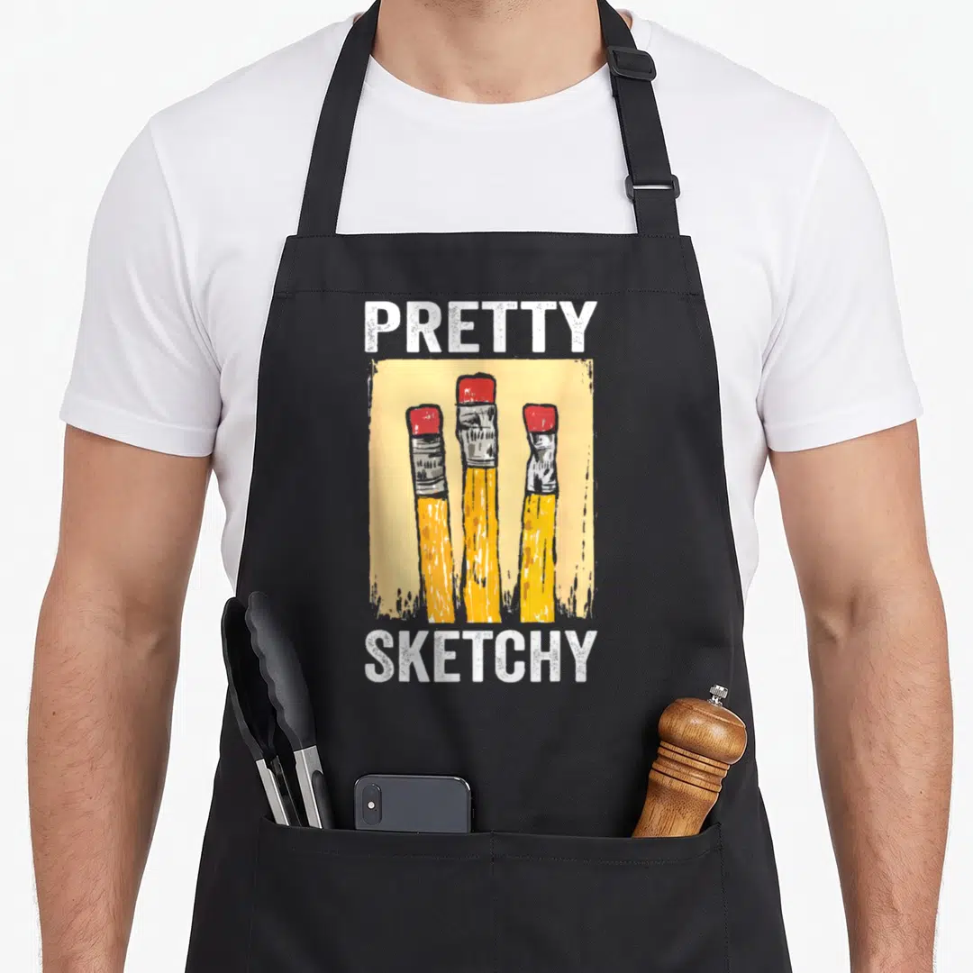 Pretty paint apron - PRETTY SKETCHY text above three yellow pencils with red erasers in cartoon style — shown on a black cotton canvas apron against a white background
