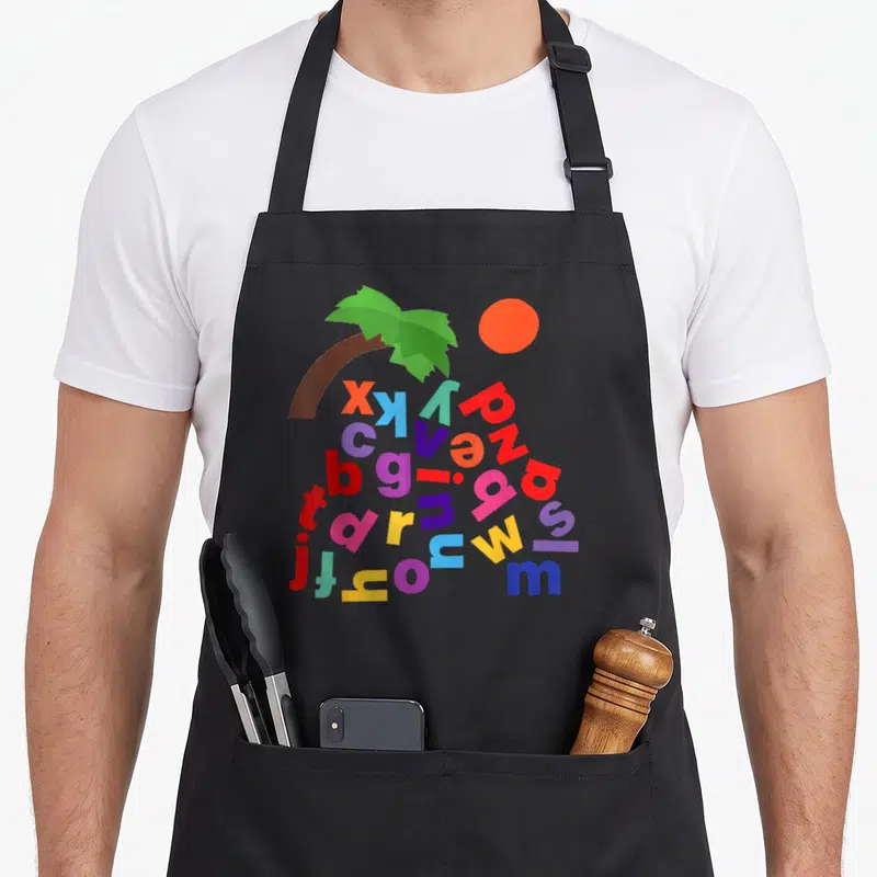 Alphabet tree apron - Cartoon palm tree with scattered red blue purple yellow and green lowercase letters under fronds — shown on a black cotton canvas apron against a white background