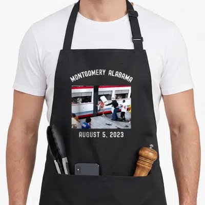 Montgomery alabama apron - Arched text MONTGOMERY ALABAMA above photo of people by transit vehicle, straight AUGUST 5 — shown on a black cotton canvas apron against a white background
