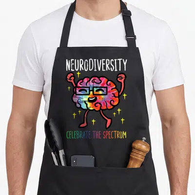 Neurodiversity autism acceptance apron - Rainbow cartoon brain with glasses raising fists surrounded by stars and text — shown on a black cotton canvas apron against a white background