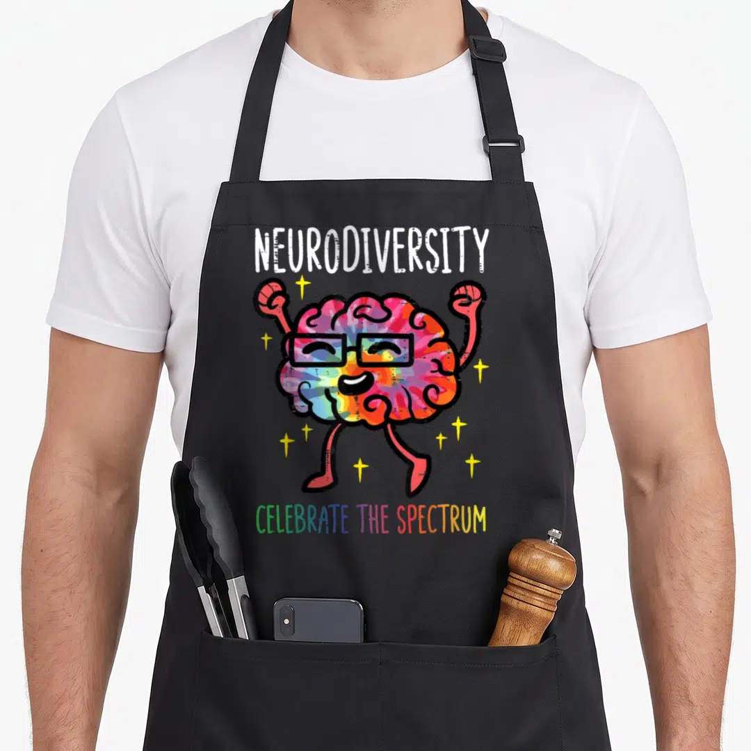 Neurodiversity autism acceptance apron - Rainbow cartoon brain with glasses raising fists surrounded by stars and text — shown on a black cotton canvas apron against a white background