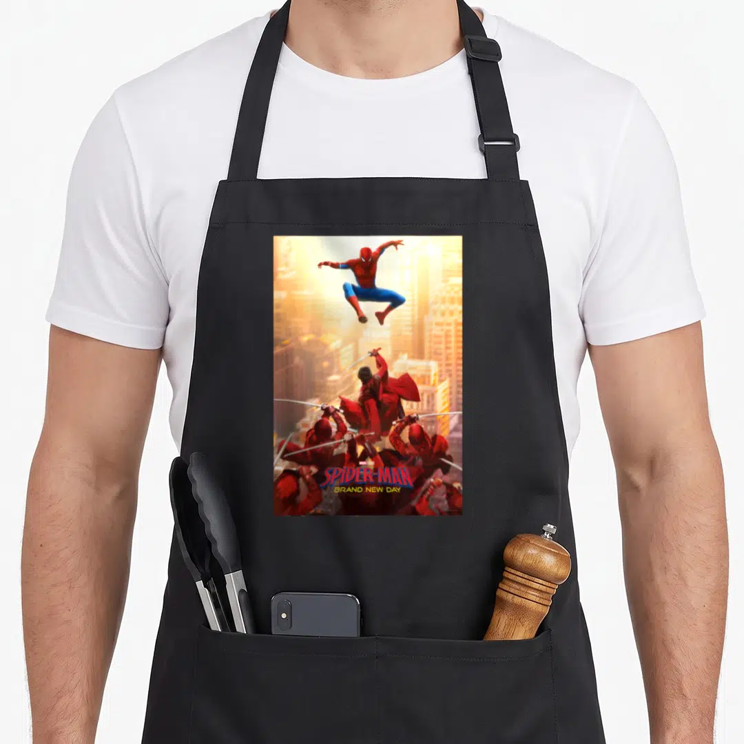 Studio boy spider apron - Spider-Man jumping above Hand Ninjas with red blue orange yellow text stacked at bottom — shown on a black cotton canvas apron against a white background