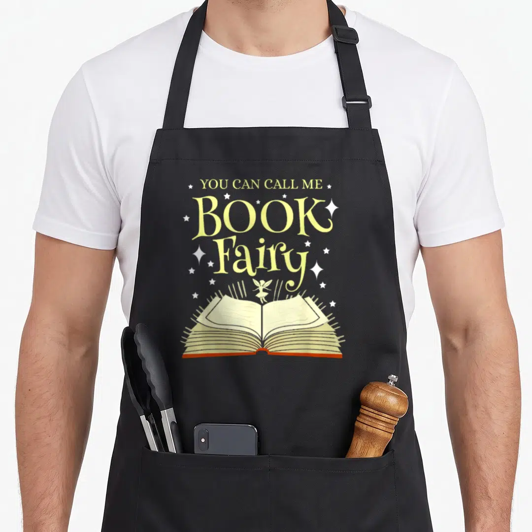 Call fairy apron - Book Fairy text and fairy standing on open book with stars — shown on a black cotton canvas apron against a white background