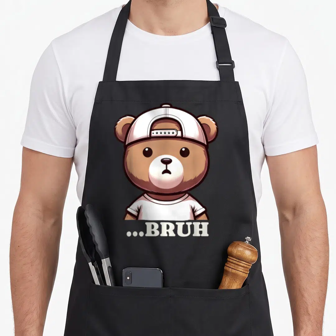 Meme hip aprons - Brown cartoon bear in white cap and shirt above white ...BRUH text — shown on a black cotton canvas apron against a white background