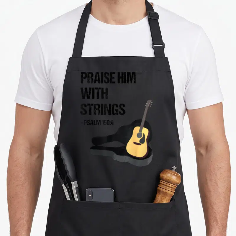 Guitar player christian apron - Stacked Praise Him With Strings text beside yellow acoustic guitar leaning on black case — shown on a black cotton canvas apron against a white background