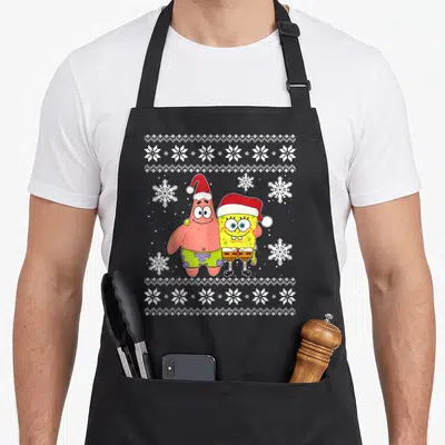 Patrick holiday christmas aprons - Two cartoon characters wearing red Santa hats standing side-by-side amidst white — shown on a black cotton canvas apron against a white background
