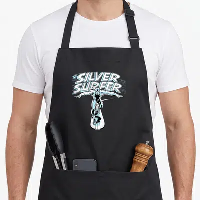 Fantastic surfer apron - THE SILVER, SURFER text arched over character standing on board in silver blue white — shown on a black cotton canvas apron against a white background