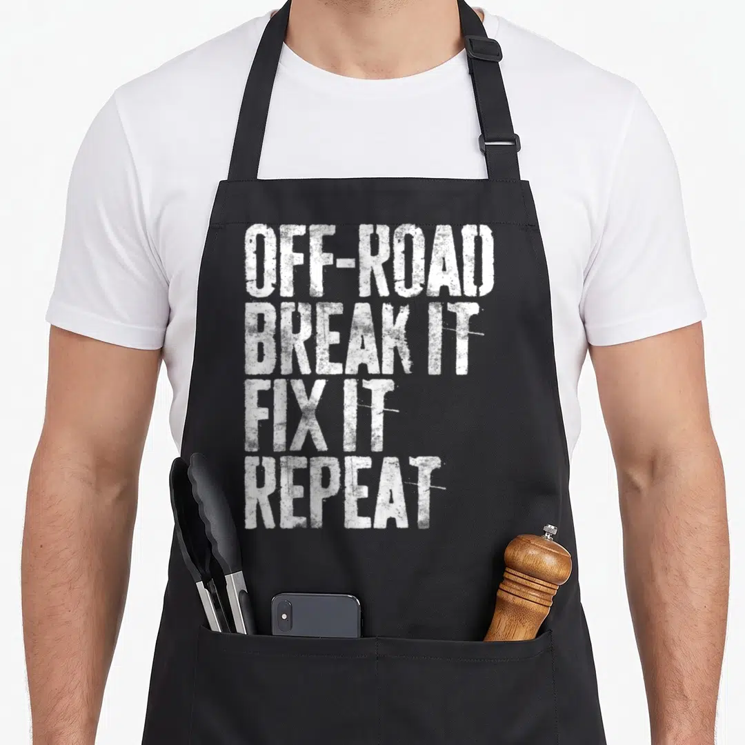 Break road apron - White stacked text reading OFF-ROAD BREAK IT FIX IT REPEAT on black fabric — shown on a black cotton canvas apron against a white background