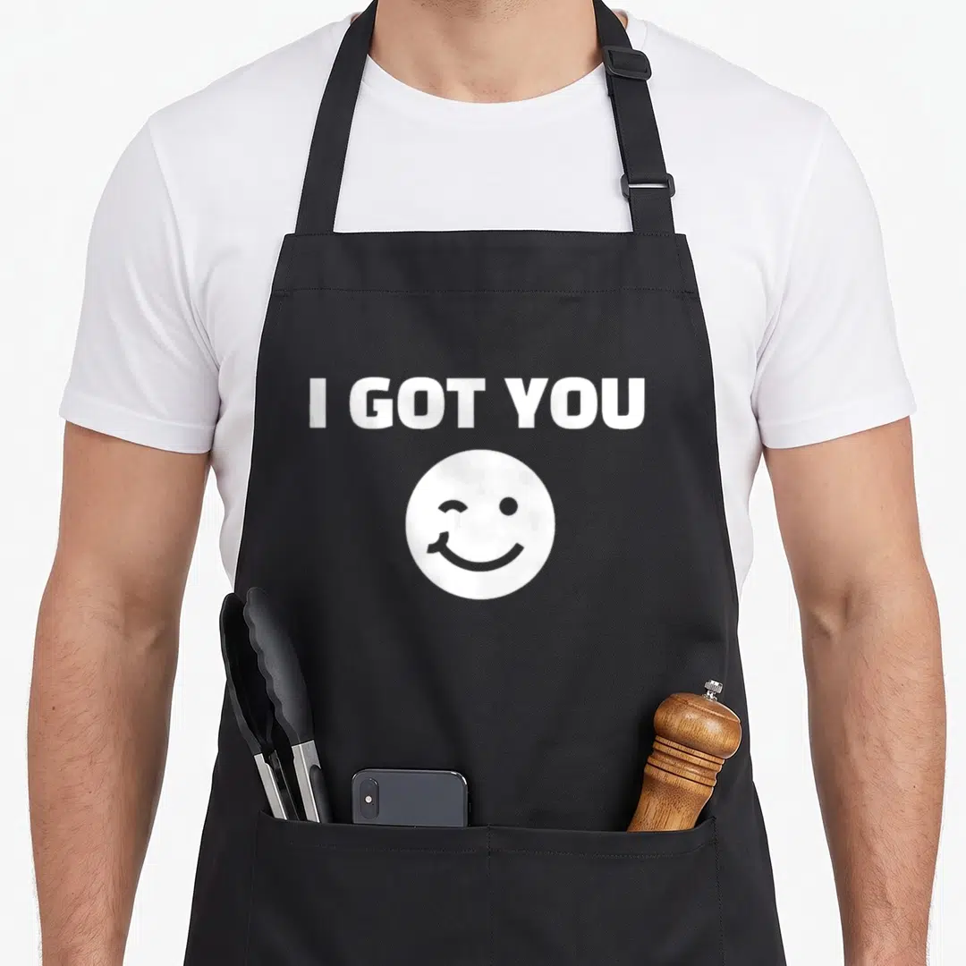 Motivation cartoon apron - White I GOT YOU text above a winking smiley face icon — shown on a black cotton canvas apron against a white background