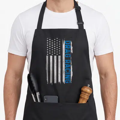Drag racing american flag apron - Distressed white blue USA flag with vertical blue drag racing text — shown on a black cotton canvas apron against a white background
